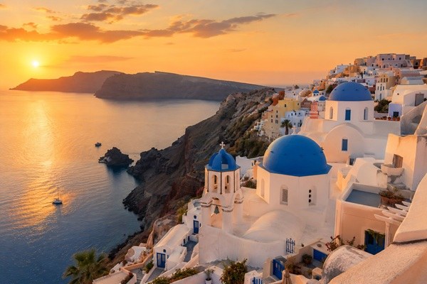 Santorinis hvide huse og blå kupler ved solnedgang over calderaen